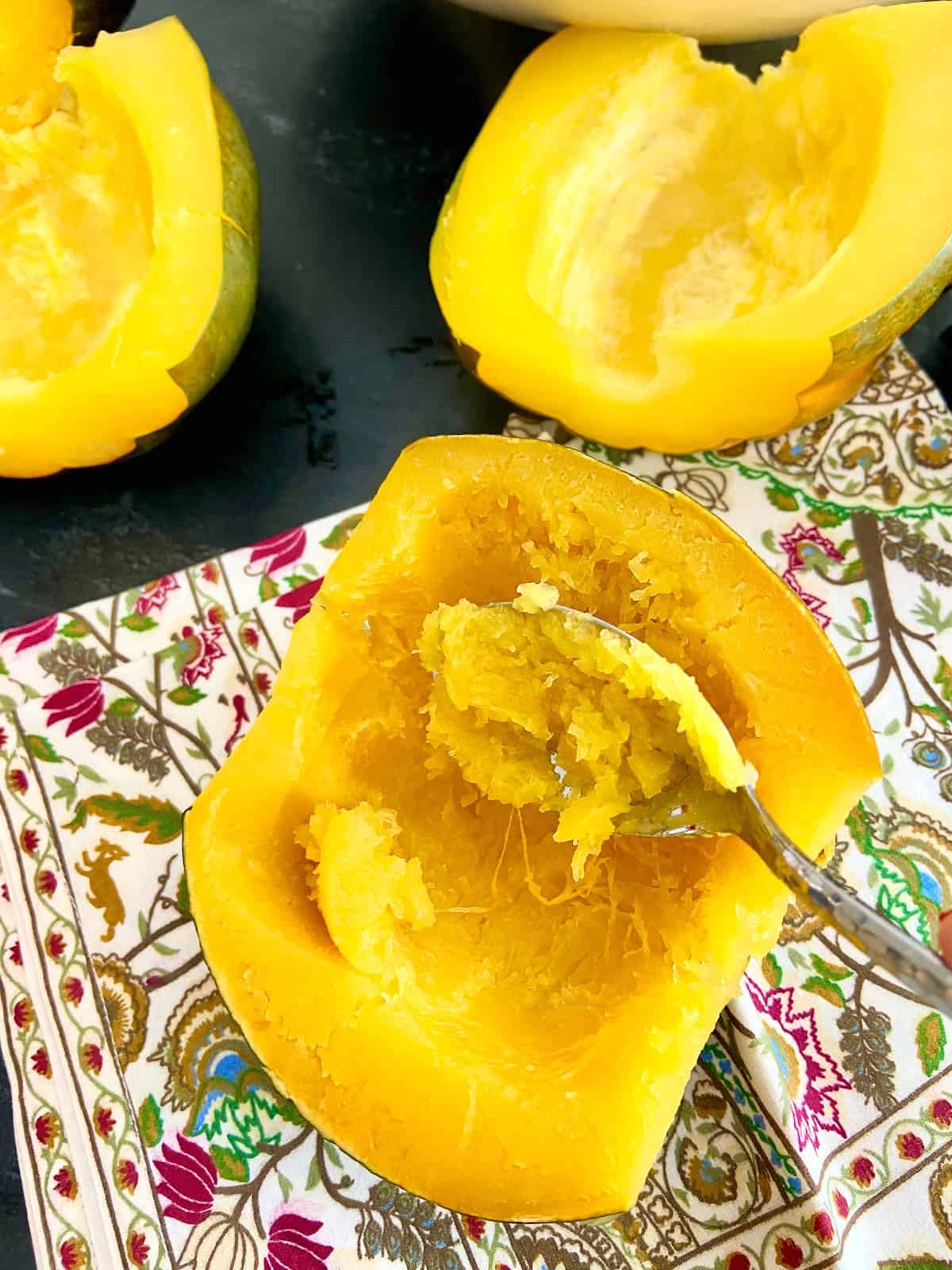 Half a cooked acorn squash with flesh being spooned out.