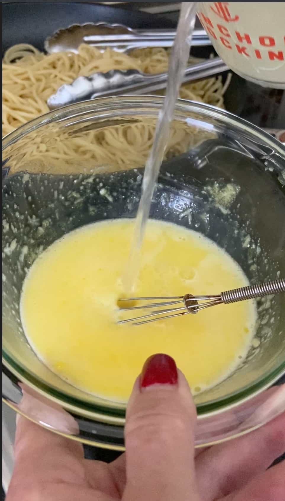 Pasta water being drizzled into egg yolk and cheese mixture.