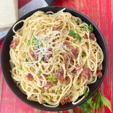 Pasta carbonara garnished with parsley and grated cheese in black bowl.