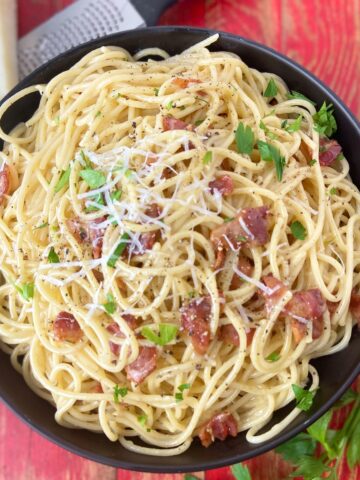 Pasta carbonara garnished with parsley and grated cheese in black bowl.