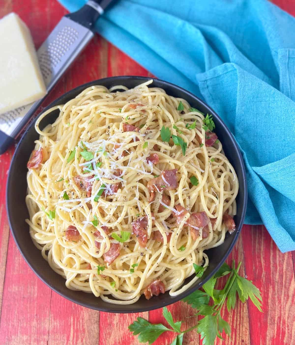 Pasta carbonara in black bowl on red wooden table.