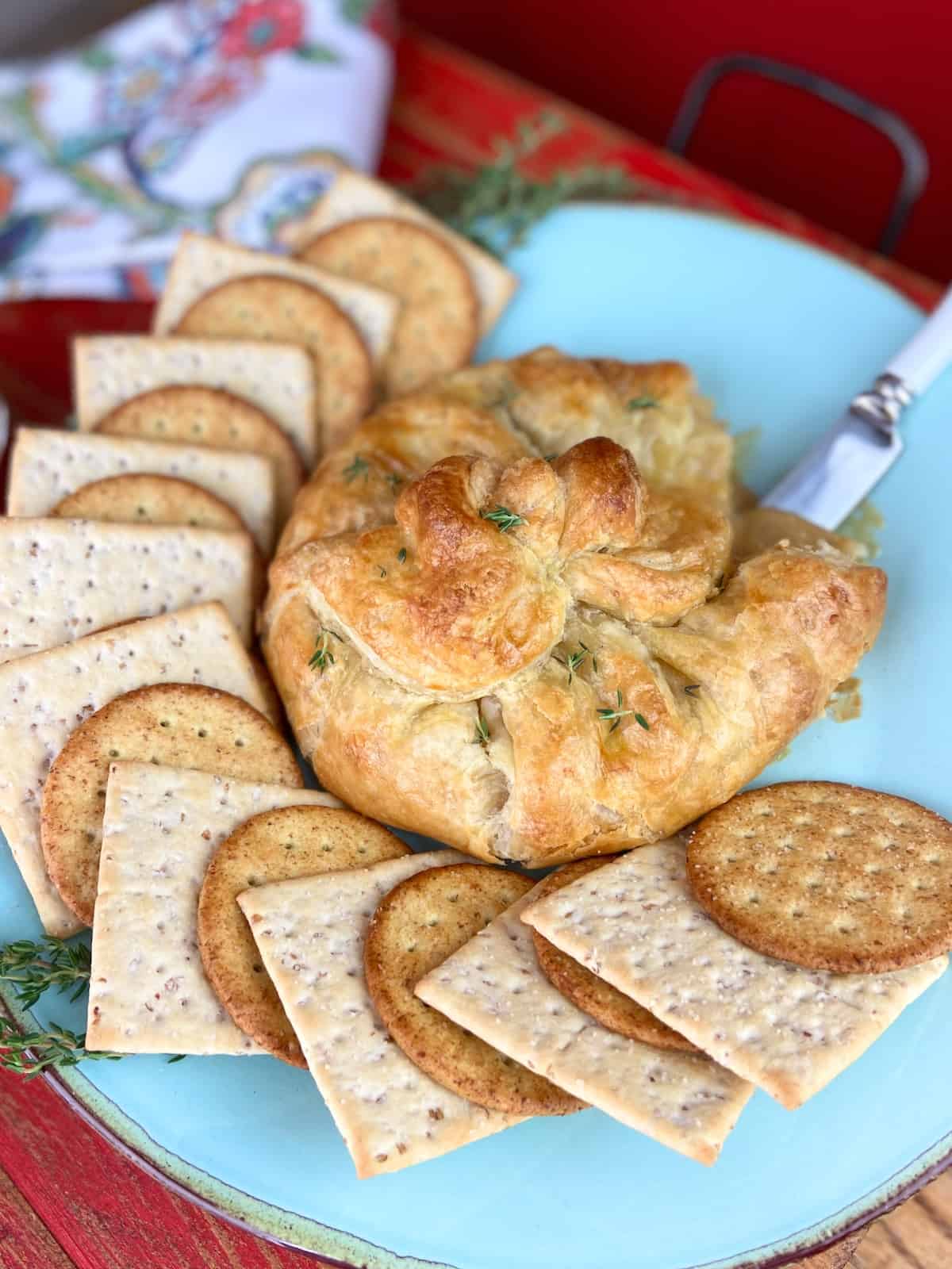 Baked brie on plate with crackers and serving knife.