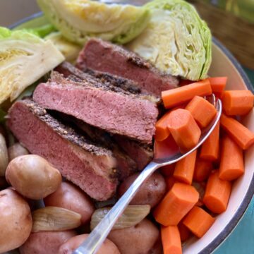 Corned Beef, cabbage, carrots and potatoes in stockpot with serving spoon.