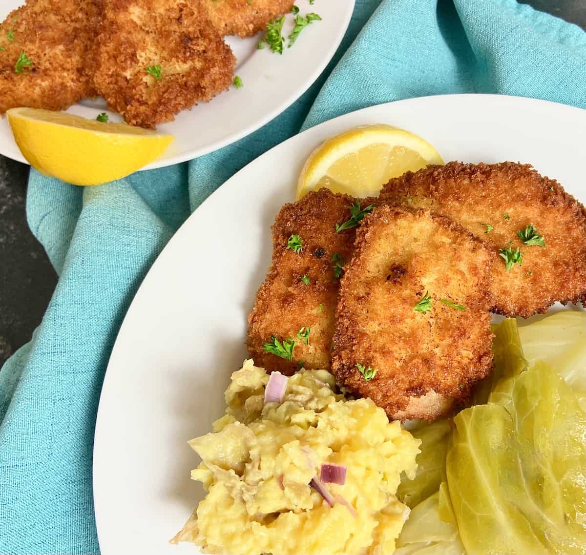 Pork schnitzel, cabbage and potato salad on white plate.