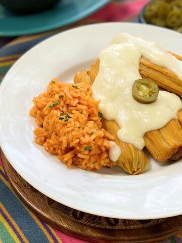 Sour cream sauce drizzled over tamales on a white plate.