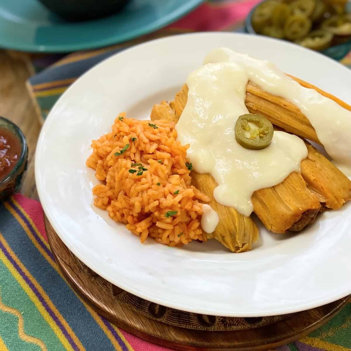 Sour cream sauce drizzled over tamales on a white plate.