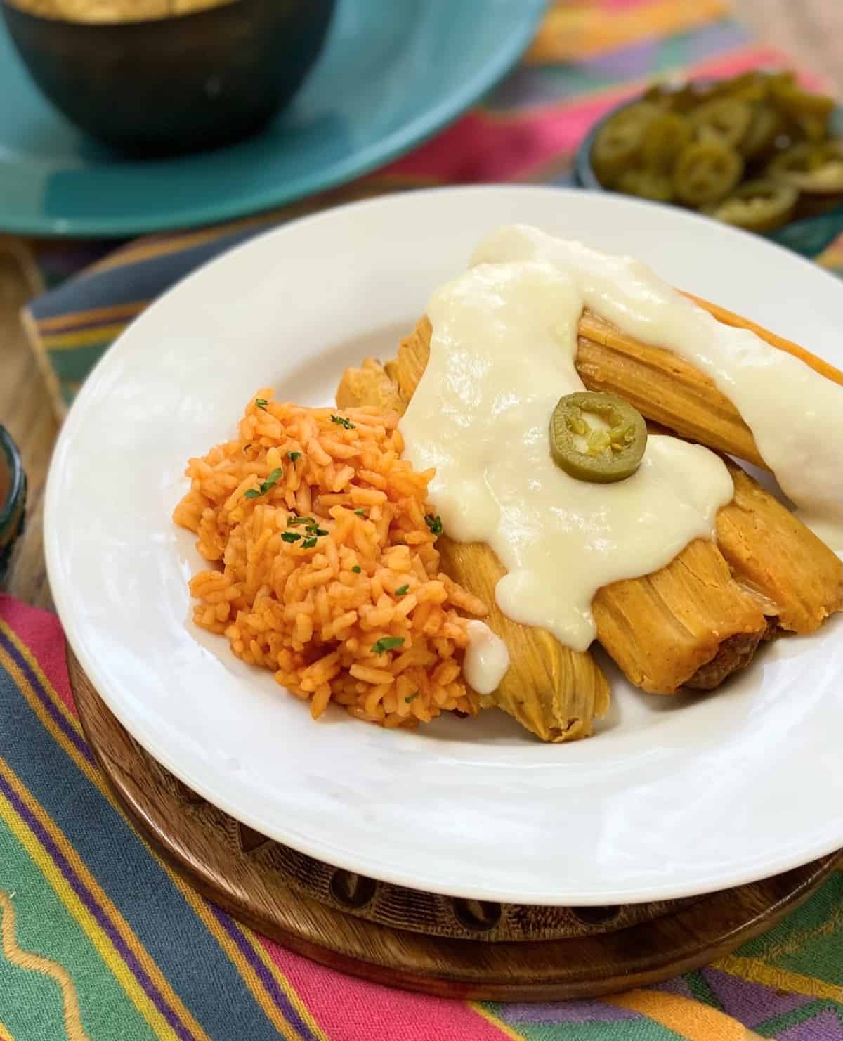 Sour Cream sauce drizzled over tamales on a white plate.