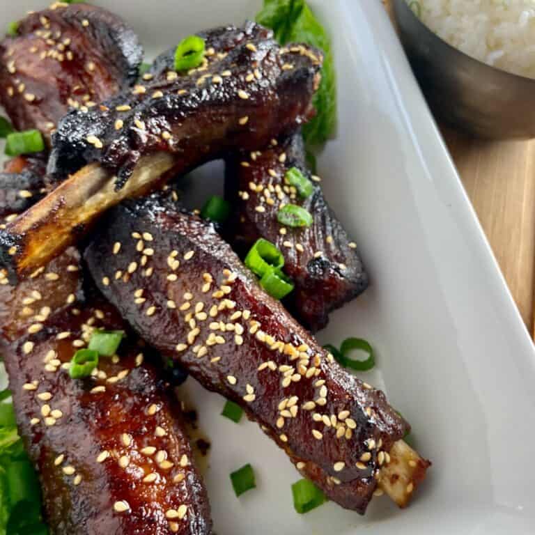 Asian sticky ribs in white serving dish garnished with chives.