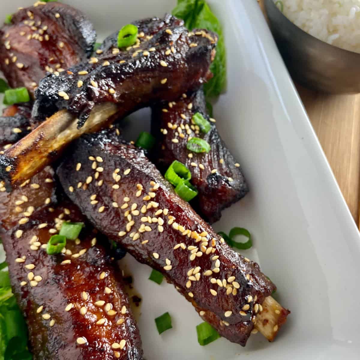 Asian sticky ribs in white serving dish garnished with chives.
