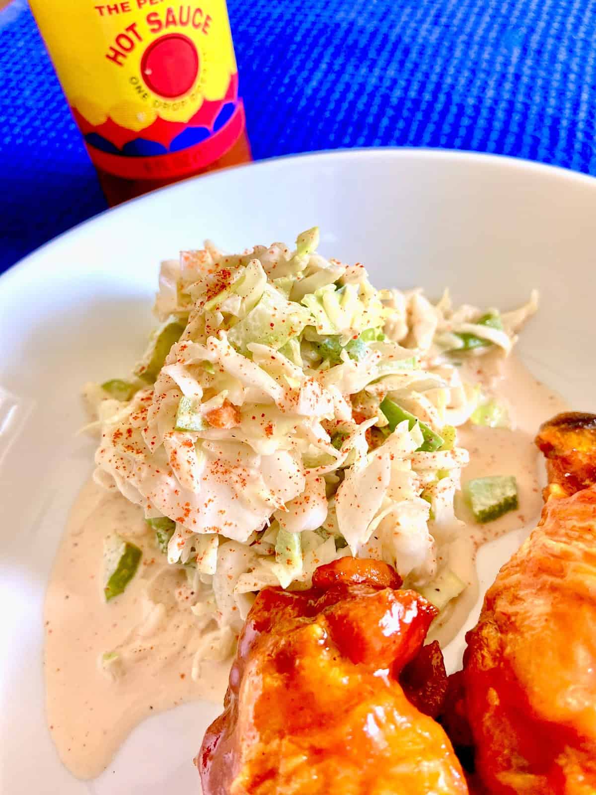 Creole coleslaw on white plate next to buffalo chicken wings.