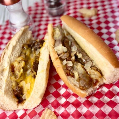 Two classic cheesesteak sandwiches on red and white checkered paper.