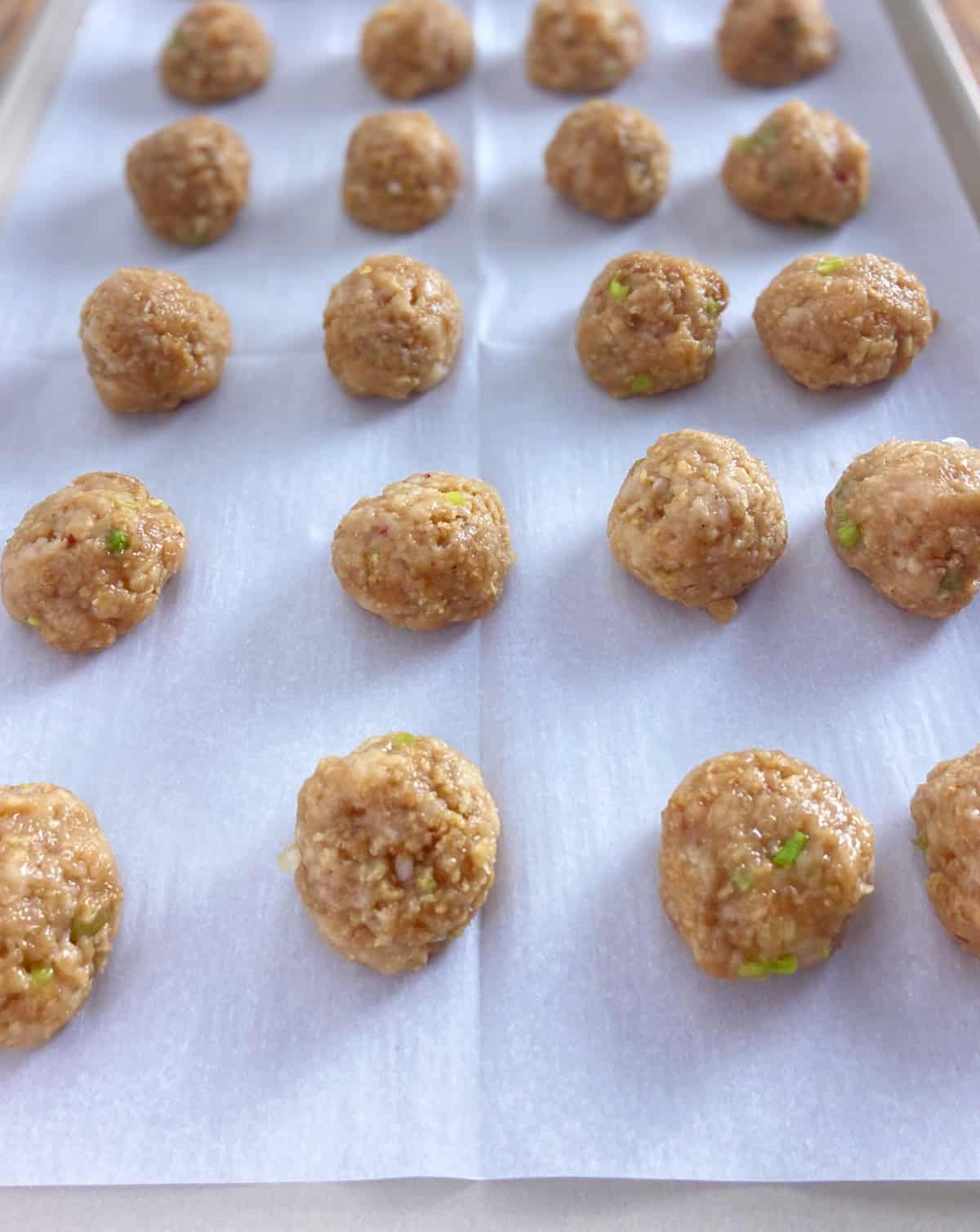 Asian chicken meatballs on parchment lined baking sheet.
