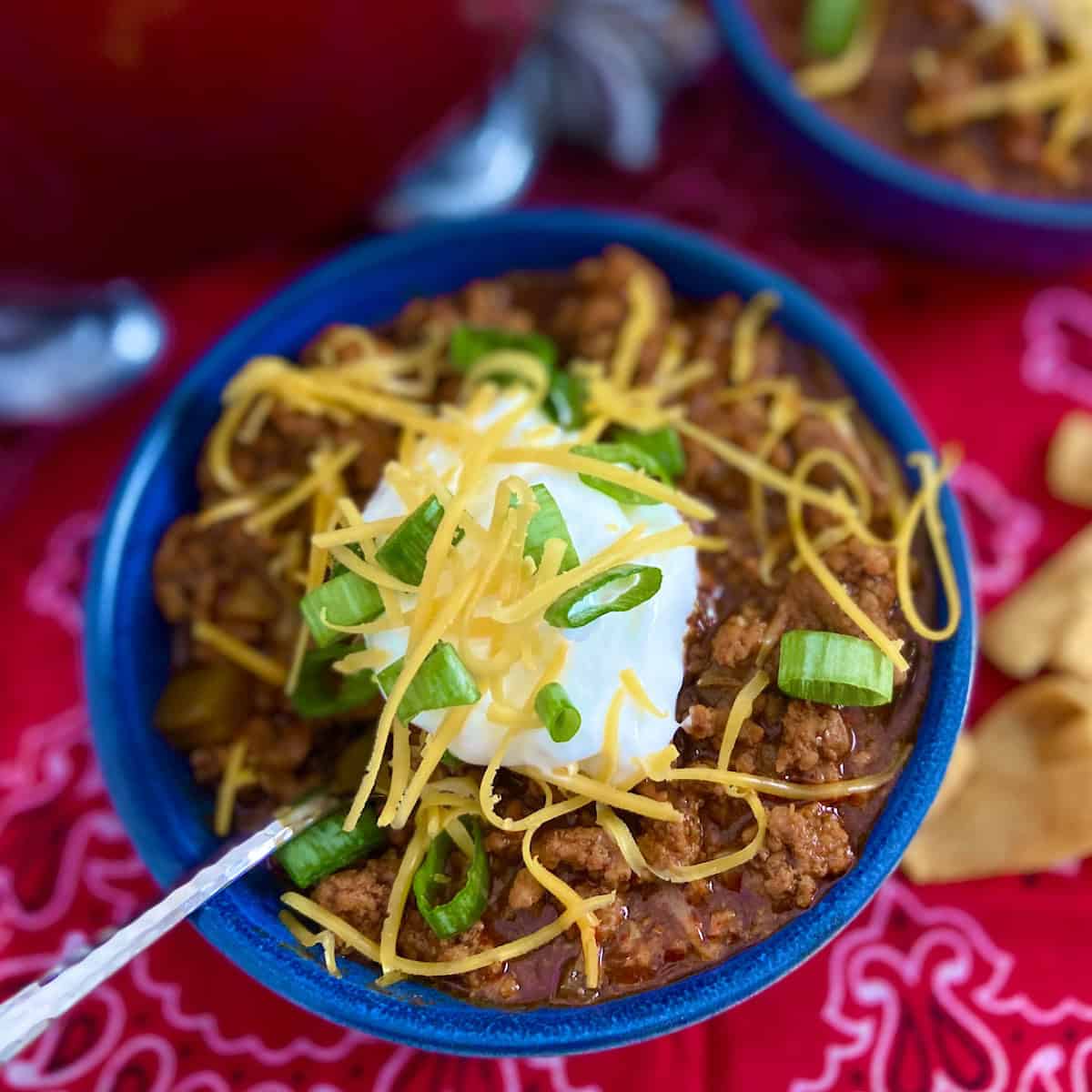 Chili in blue bowl with shredded cheddar, sour cream and green onions.