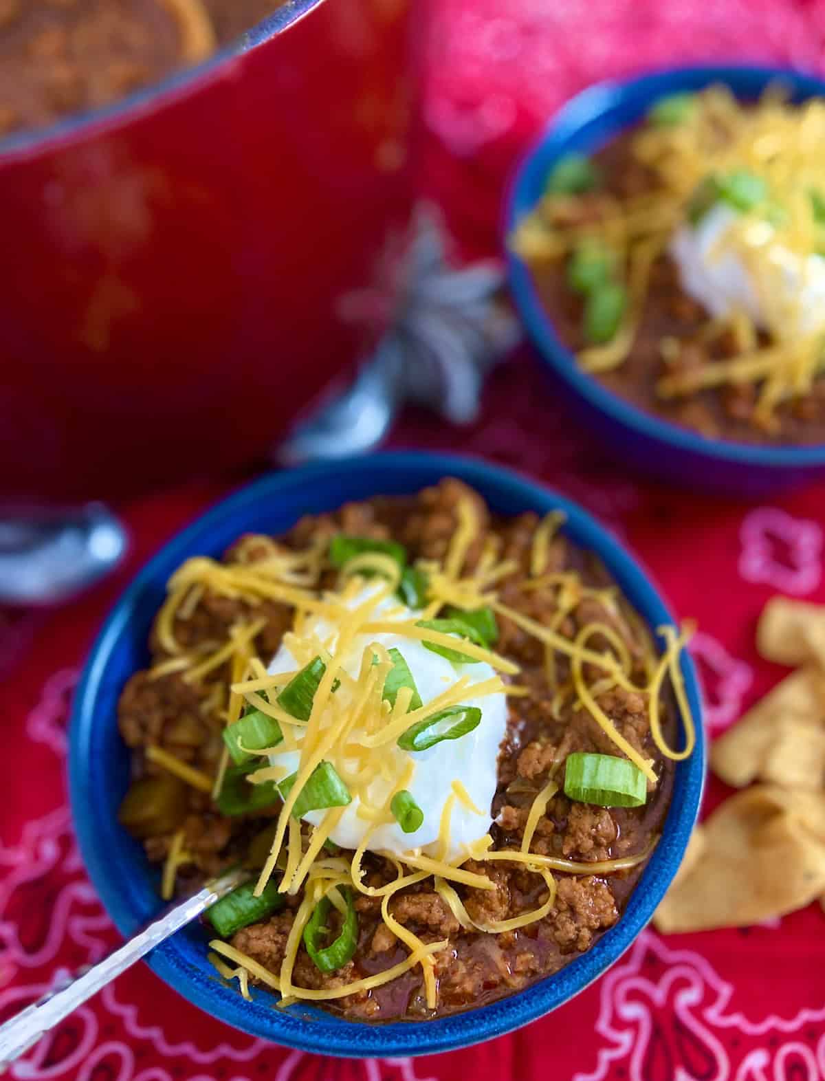 Chili in a blue bowl topped with sour cream, shredded cheddar and a dollop of sour cream.