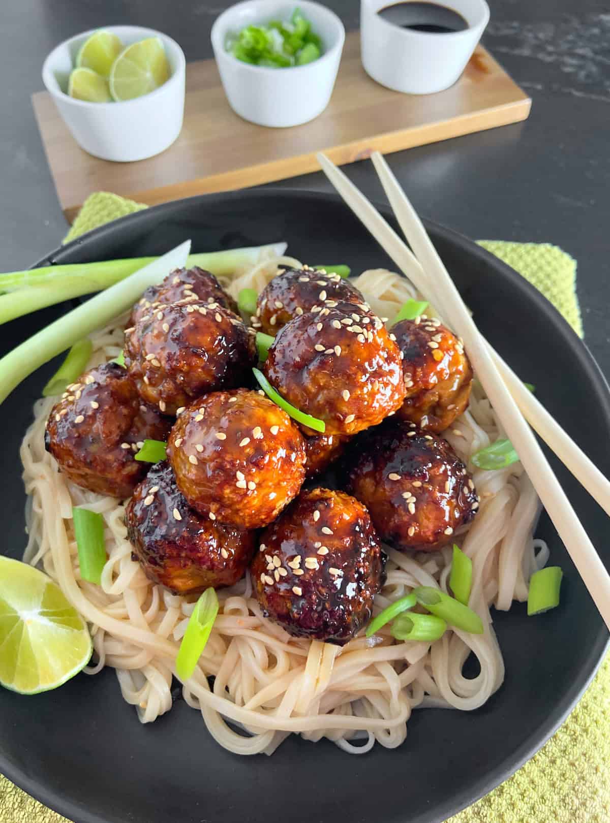 Asian chicken meatballs garnished with sesame seeds in black bowl.