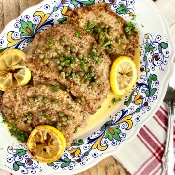 Chicken Piccata on decorative serving plate garnished with lemons and capers.
