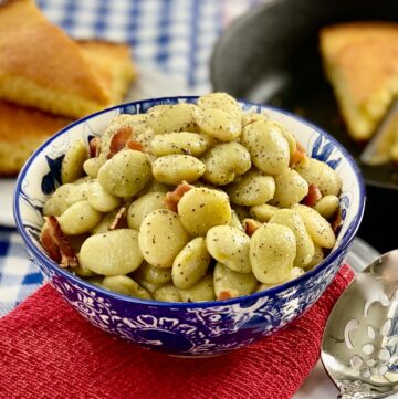 Small green lima beans in decorative blue bowl garnished with bits of bacon.