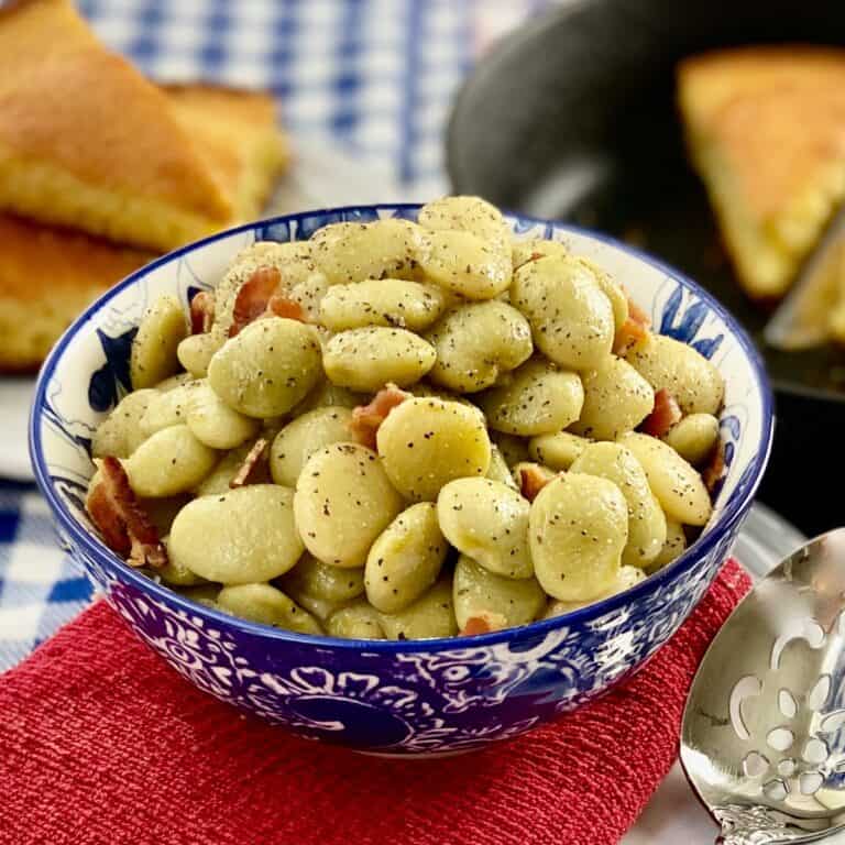 Small green lima beans in decorative blue bowl garnished with bits of bacon.