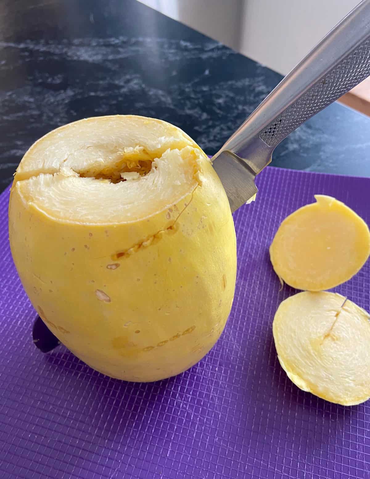 Spaghetti squash with chef's knife cutting it in half.