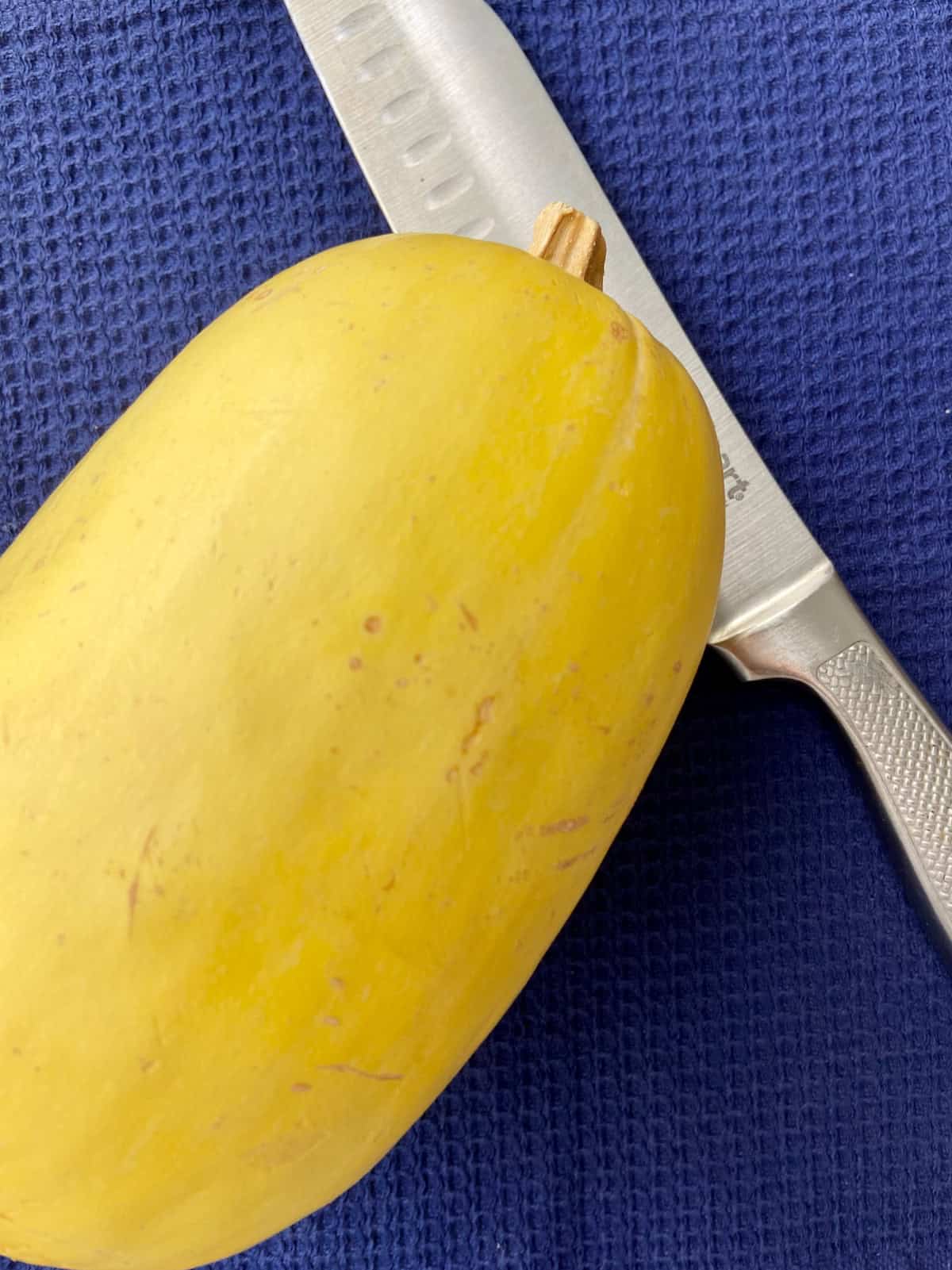 Whole spaghetti squash and chef's knife on blue table.