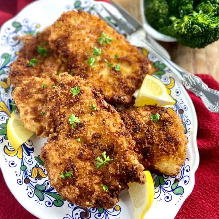 Fried chicken cutlets on decorative serving platter with lemon wedges.