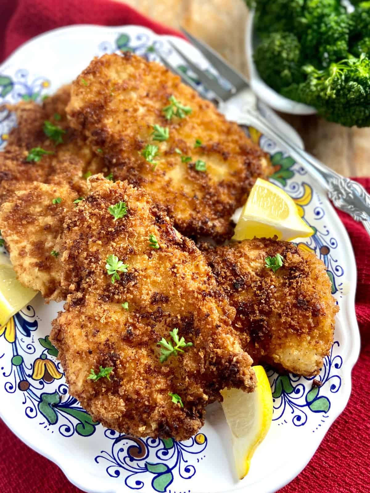 Chicken cutlets on decorative serving platter with lemon wedges.