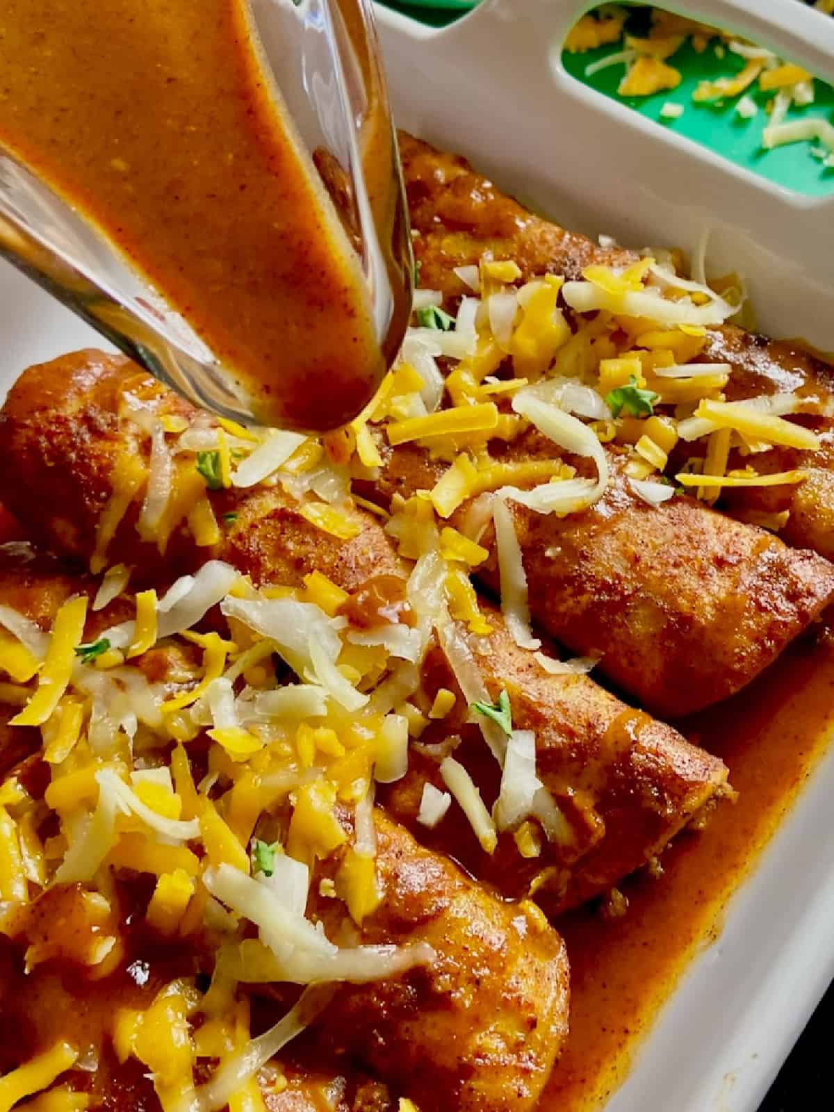 Red enchilada sauce being drizzled over cheesy enchiladas.