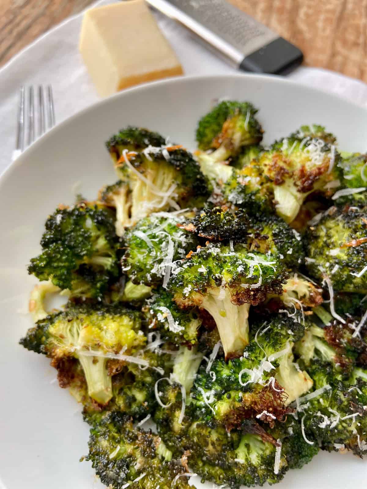 Broccoli in white bowl garnished with shredded Parmesan cheese.