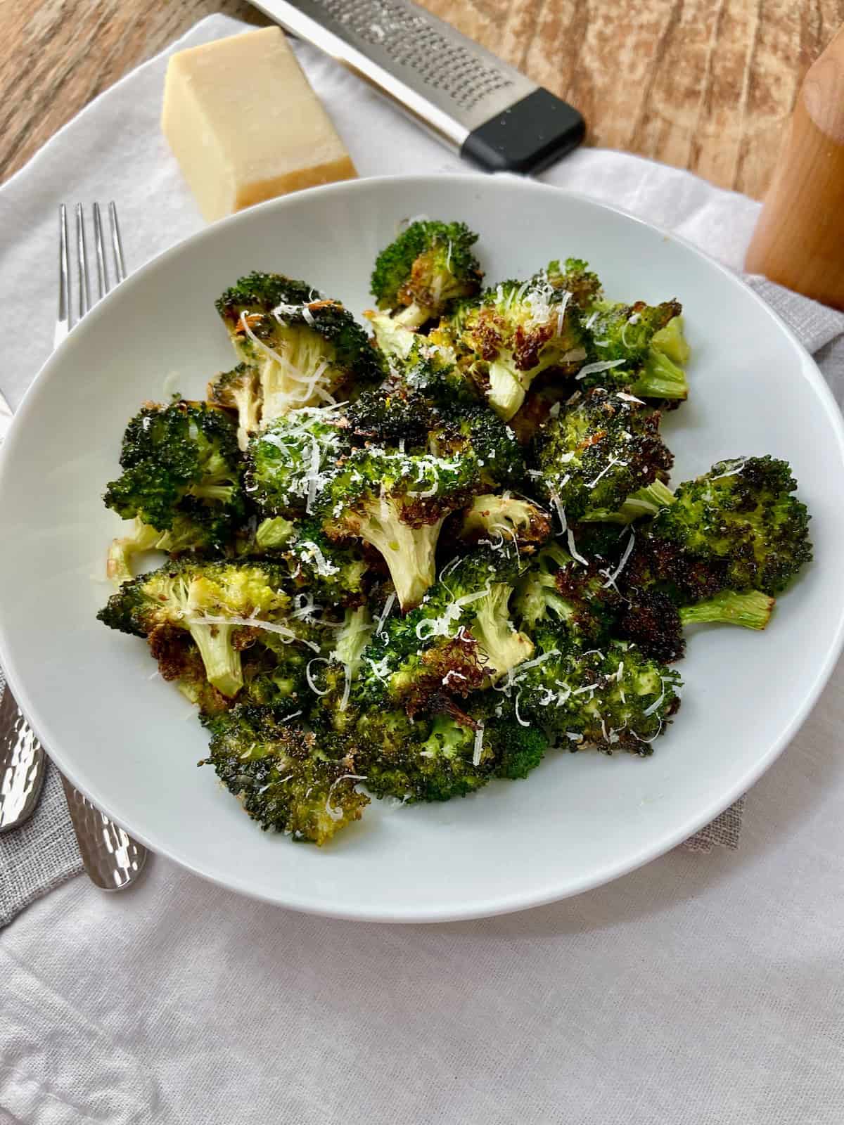 Bowl of roasted broccoli on white tablecloth.