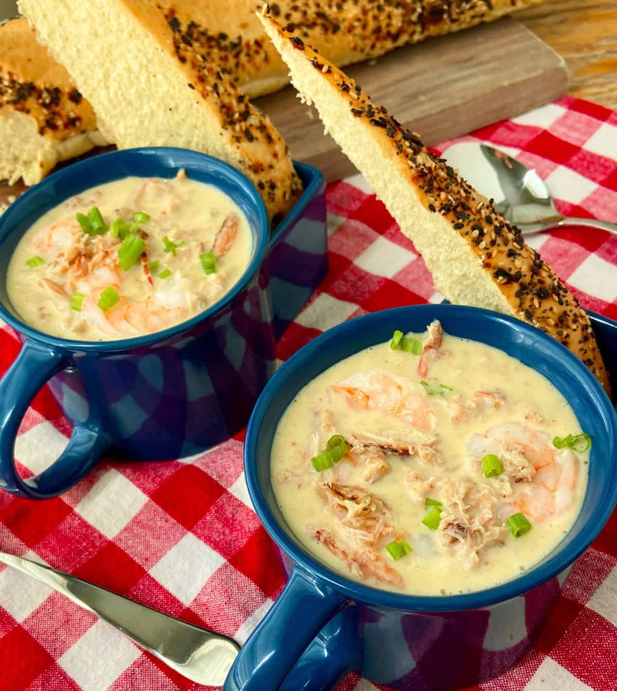Two blue bowls of bisque on red and white checkered tablecloth.