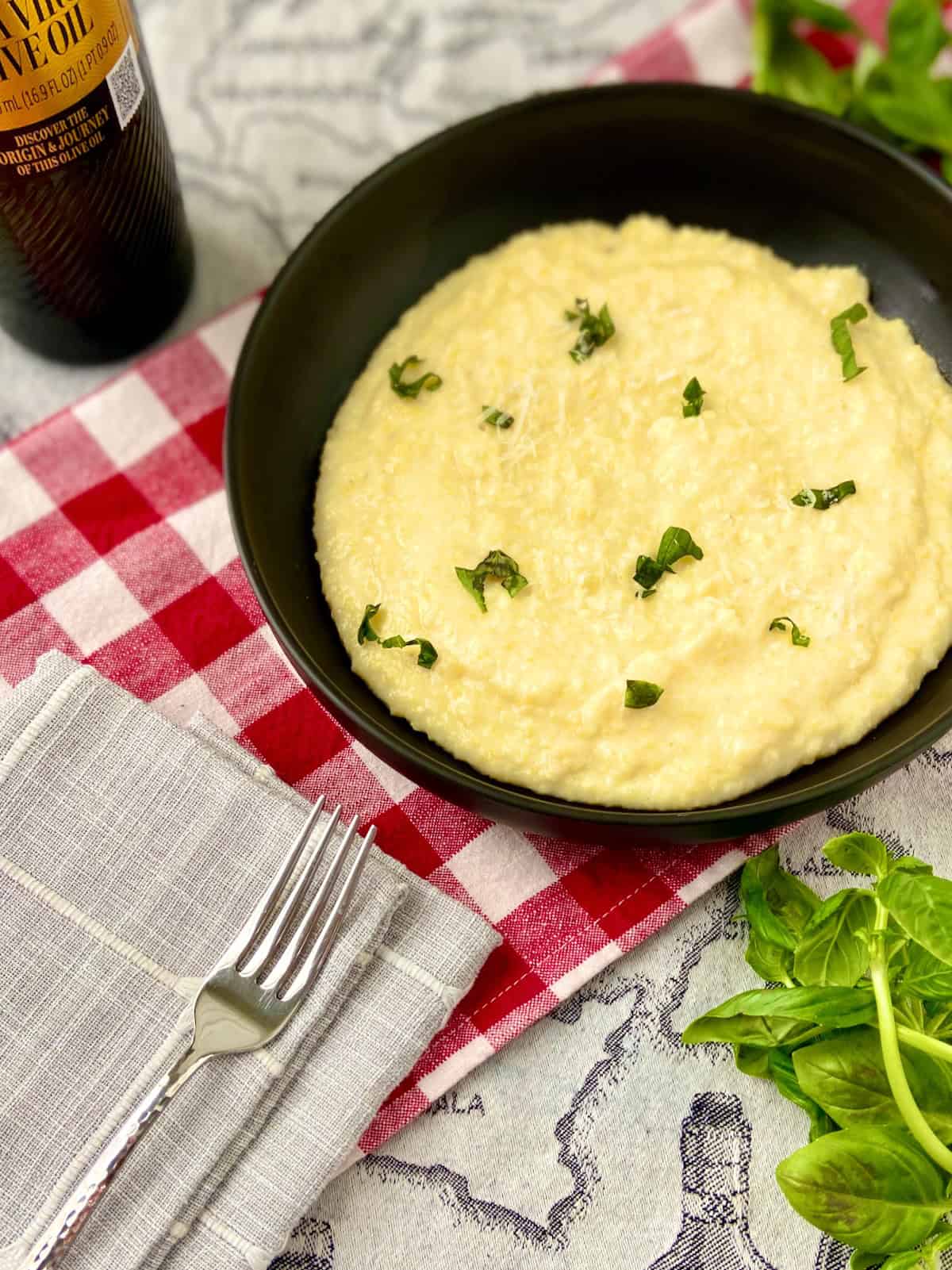 Creamy Polenta in black bowl garnished with fresh basil.