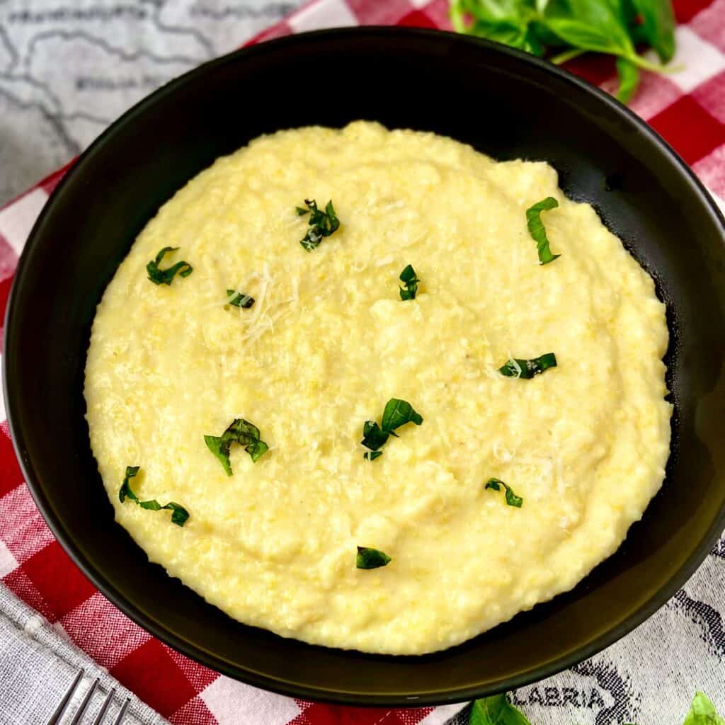 Creamy polenta in black bowl garnished with chopped basil and grated cheese.