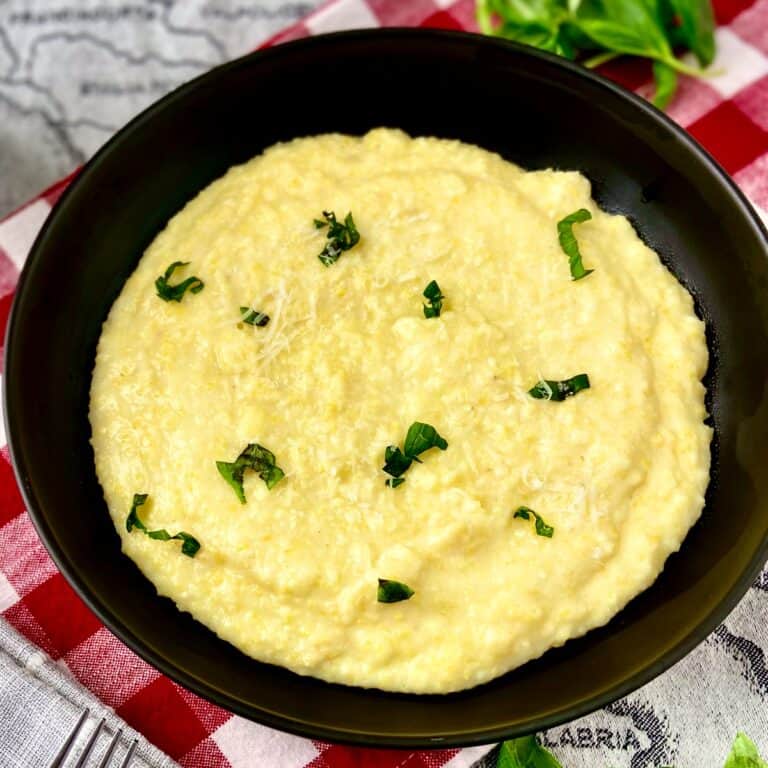 Creamy polenta in black bowl garnished with chopped basil and grated cheese.
