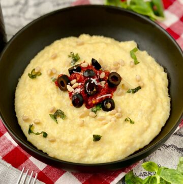 Polenta in black bowl topped with sundried tomatoes, black olives and basil.
