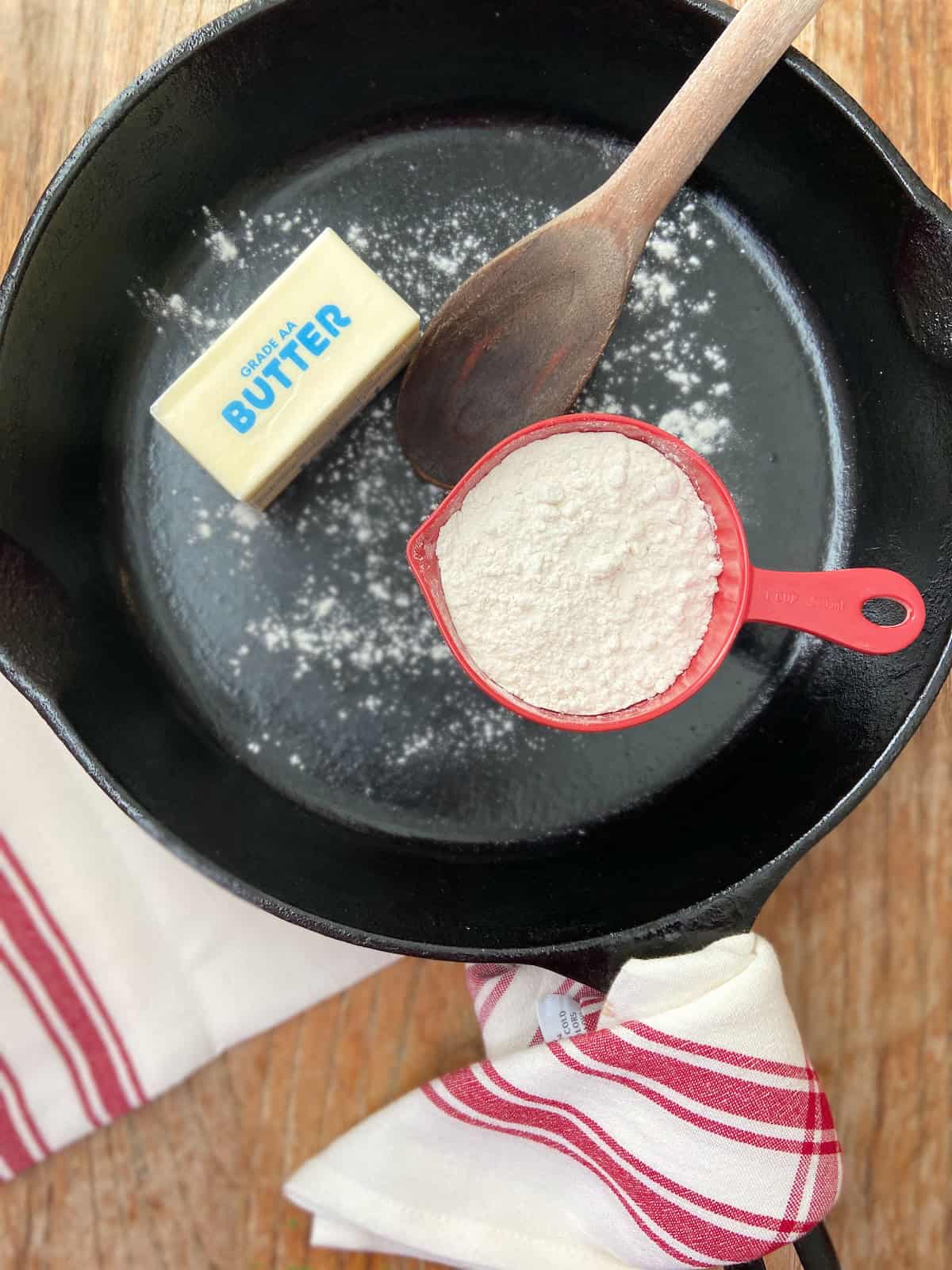 Stick of butter and cup of flour in cast iron skillet with a wooden spoon.