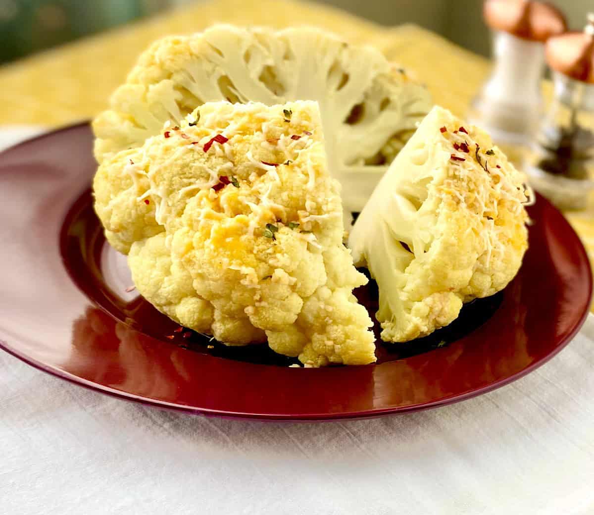 Whole roasted cauliflower with cheese cut into quarters on red plate.