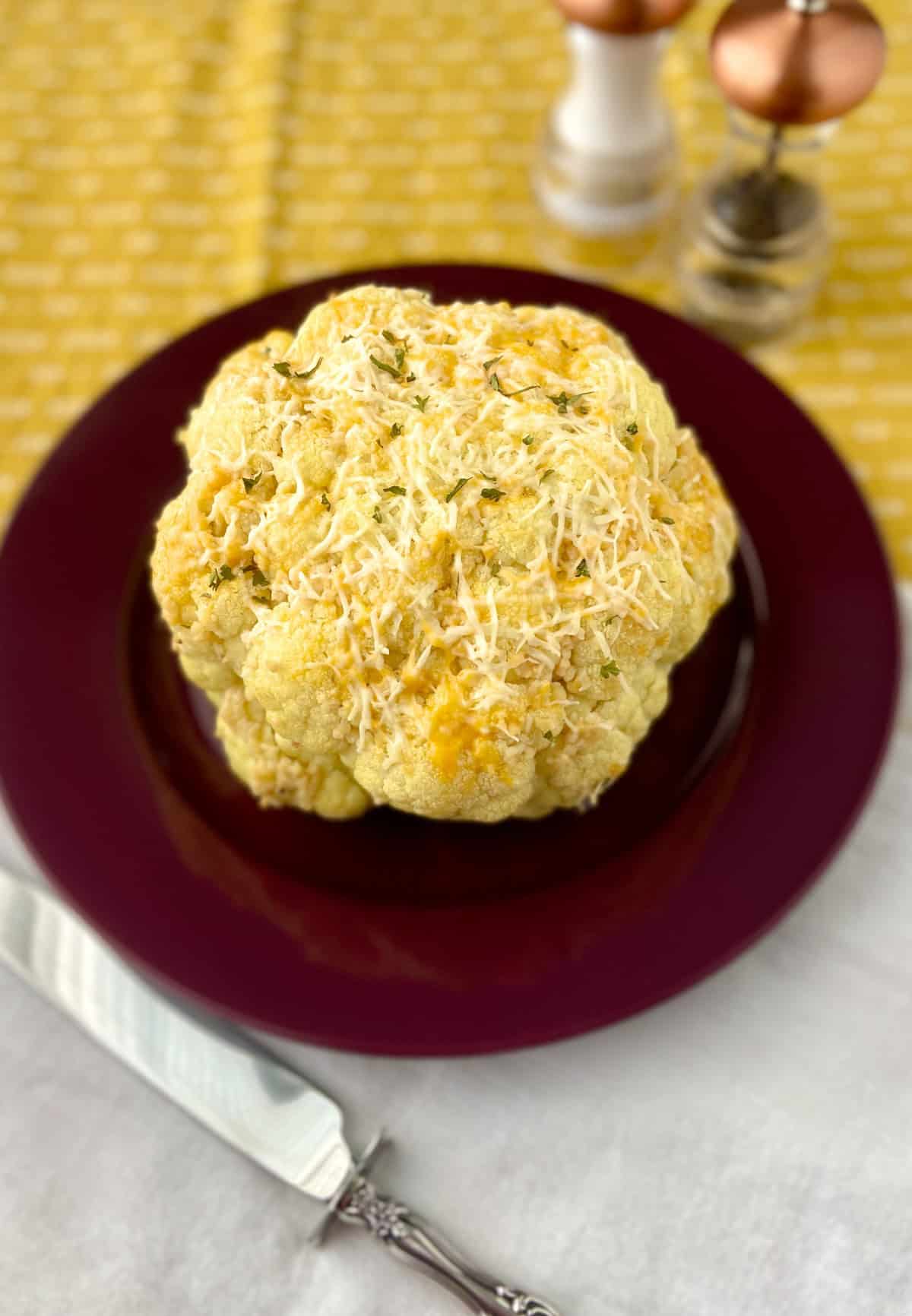 Whole roasted cauliflower with cheese on red plate.