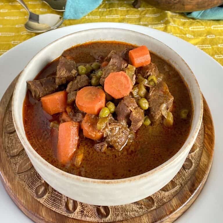 Beef stew with carrots and peas in white bowl.