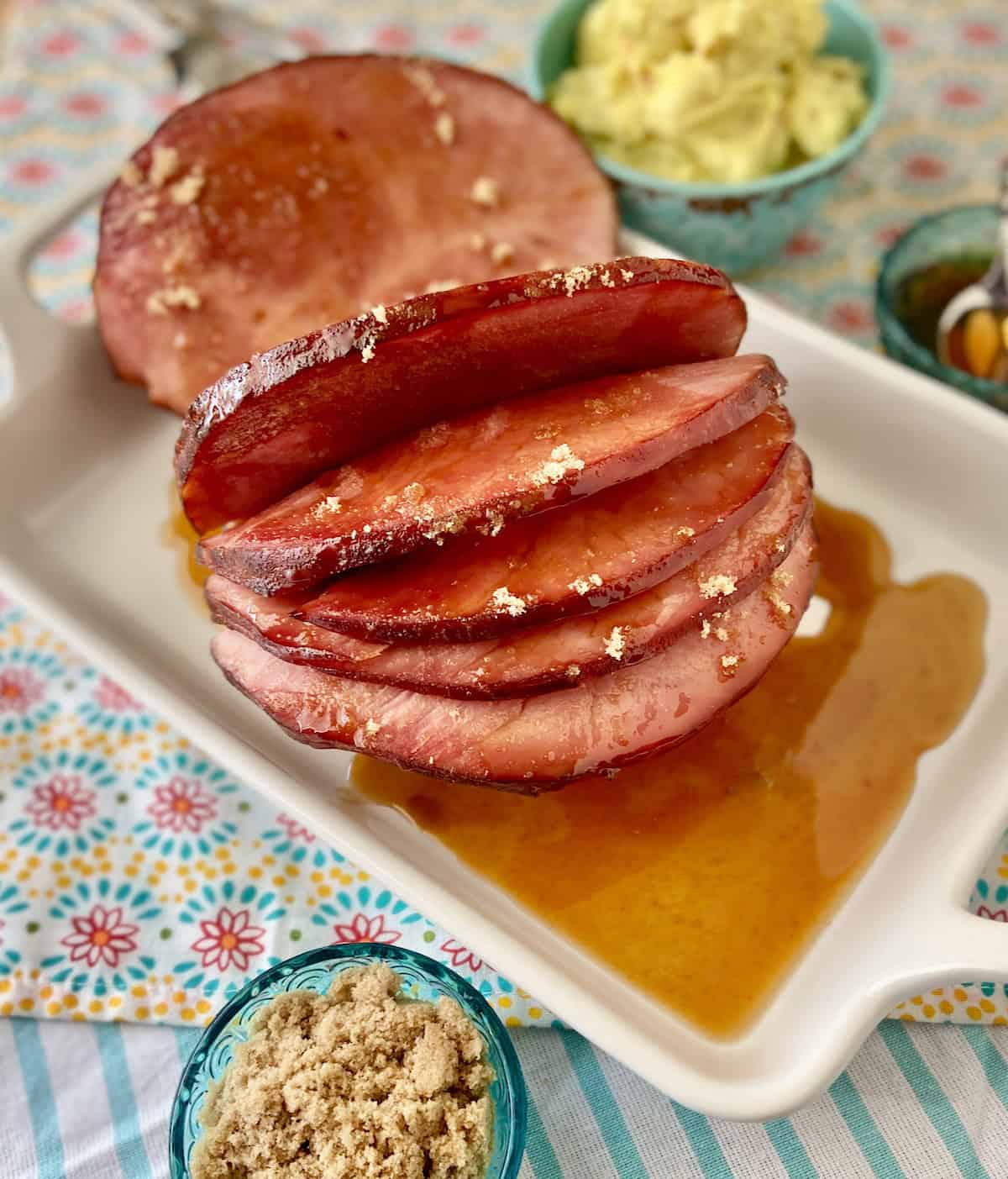 Glazed ham with sauce in white serving platter.