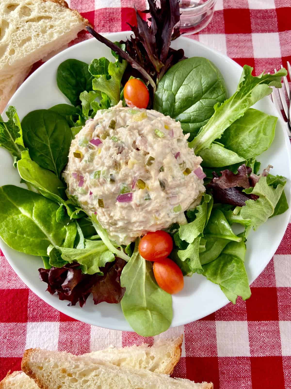 Scoop of tuna salad on a bed of greens with a few grape tomatoes.