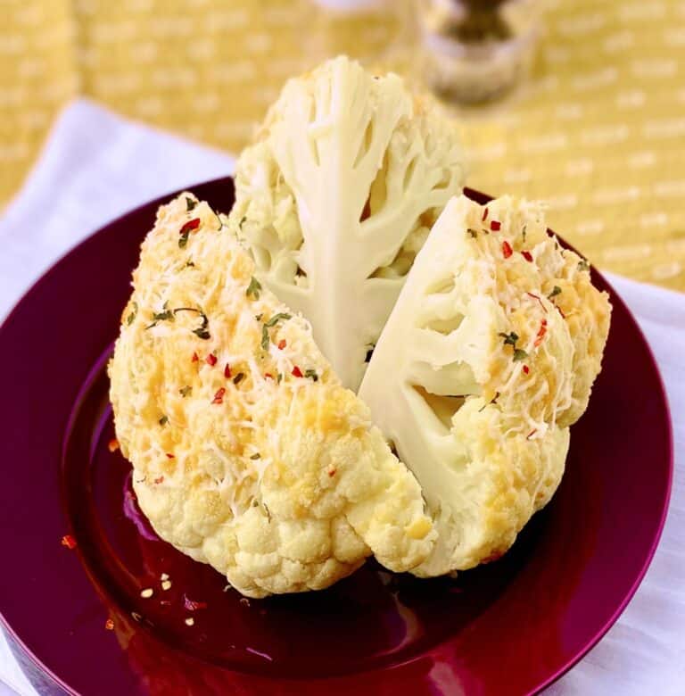 Whole roasted cauliflower on red plate.