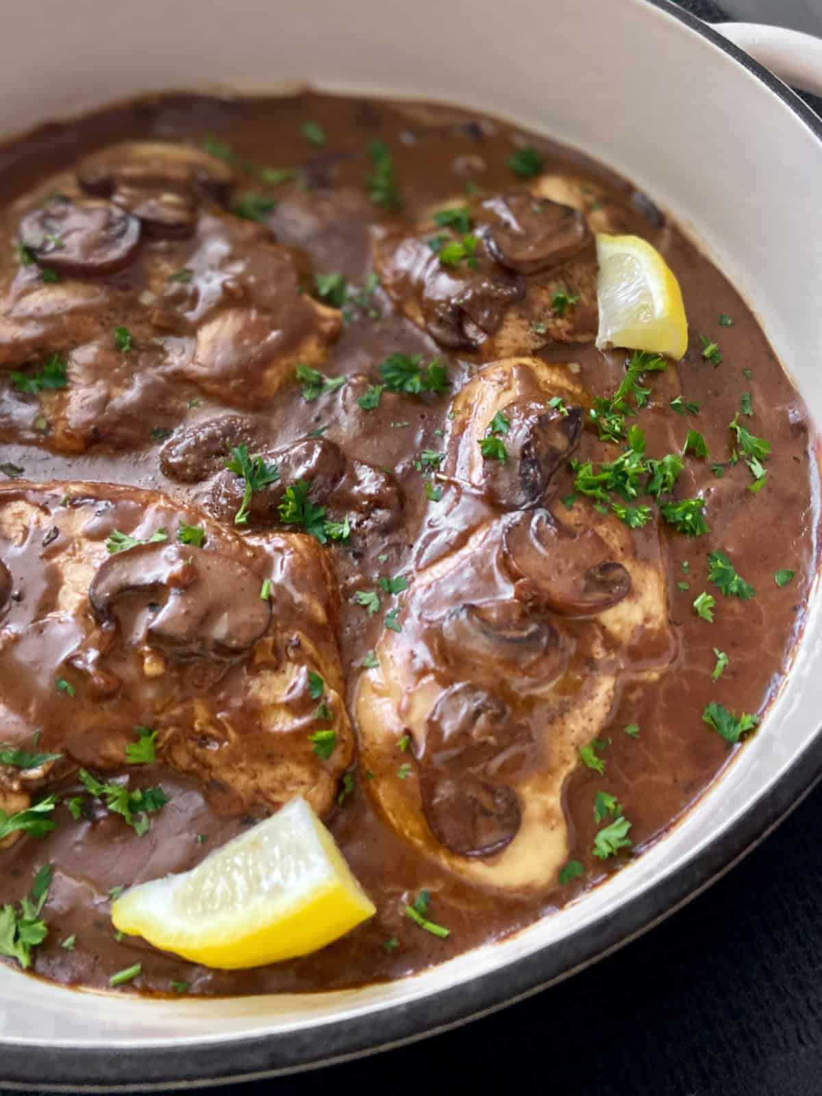 Close up image of balsamic chicken in pan with mushrooms and lemon wedges.