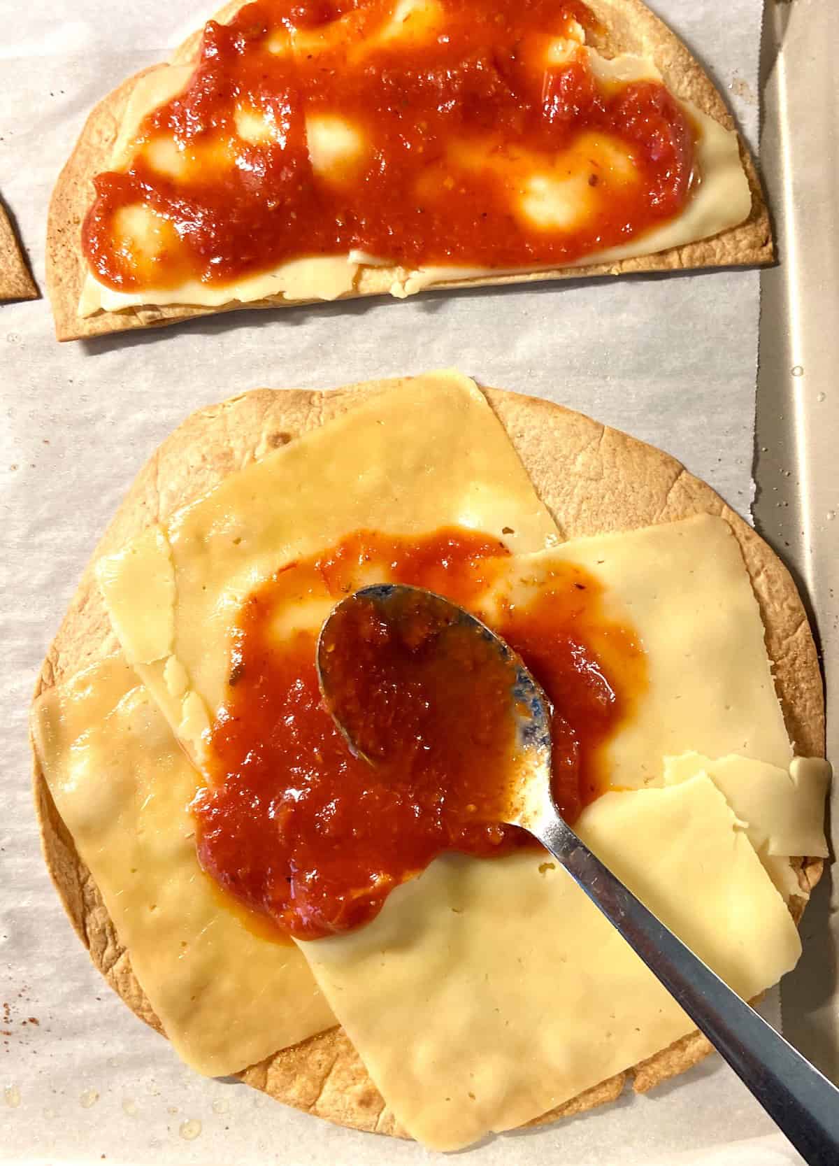 Marinara being spooned over cheese topped baked flour tortilla.