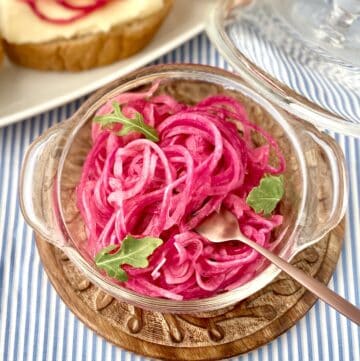Sweet pickled red onions in clear serving bowl with copper fork.