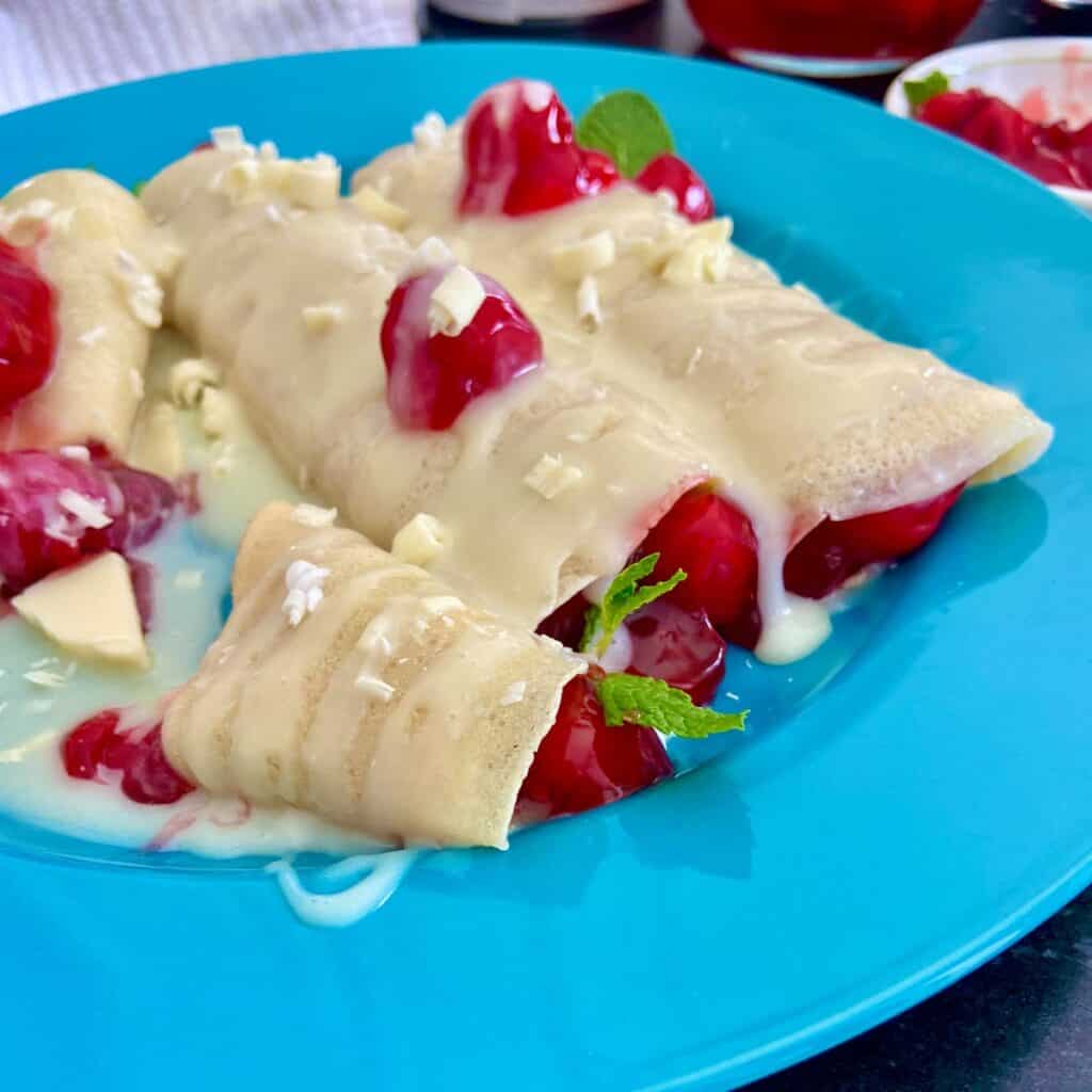 White chocolate cherry crepes on turquoise plate.