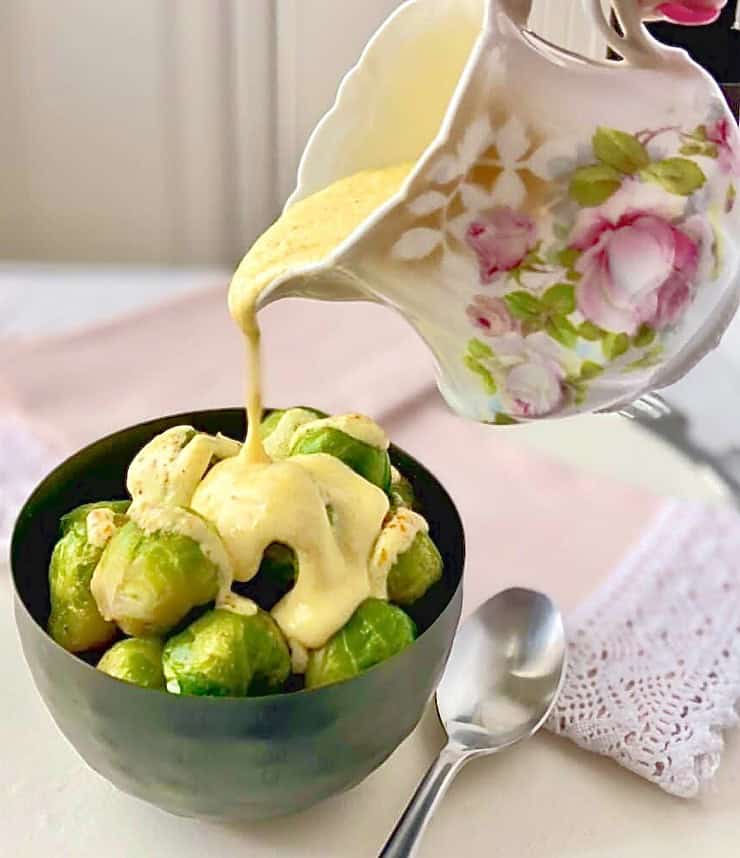 Steamed brusssels sprouts in a black bowl being drizzled with Dijon sauce.