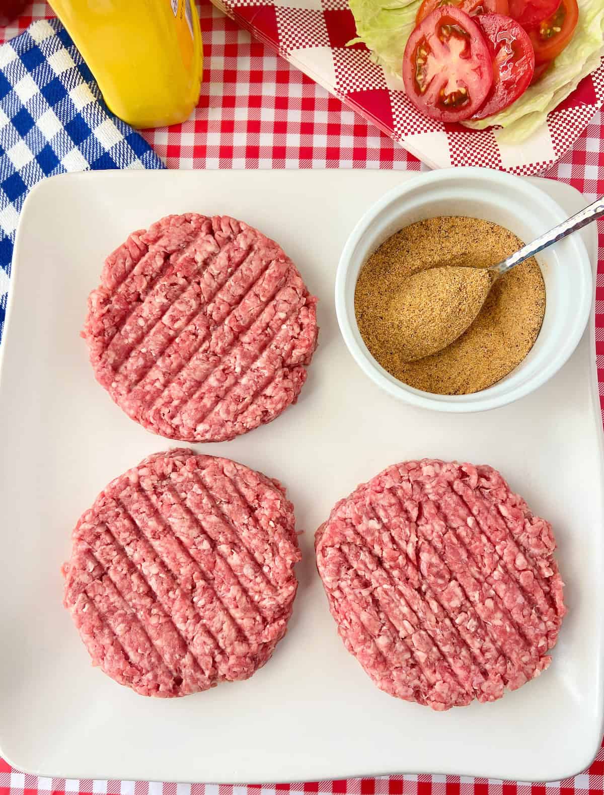 Three beef patties and a bowl of seasoning mix on white platter.