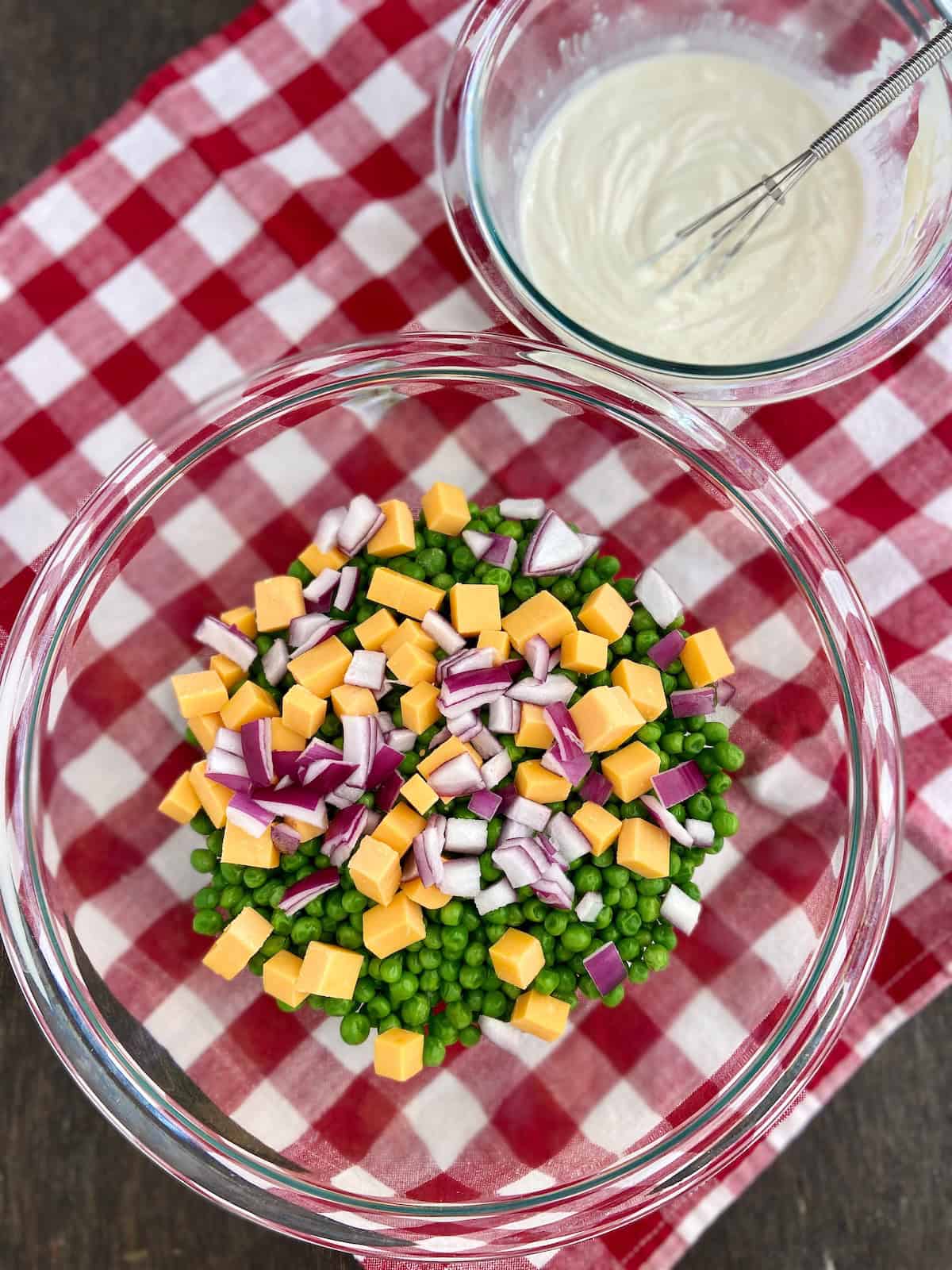 Green peas, cheddar cheese cubes and chopped red onion in clear mixing bowl.