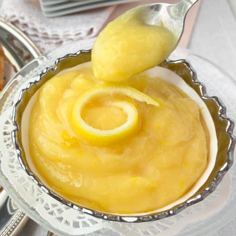 Lemon curd on a spoon in an antique silver lined serving bowl.