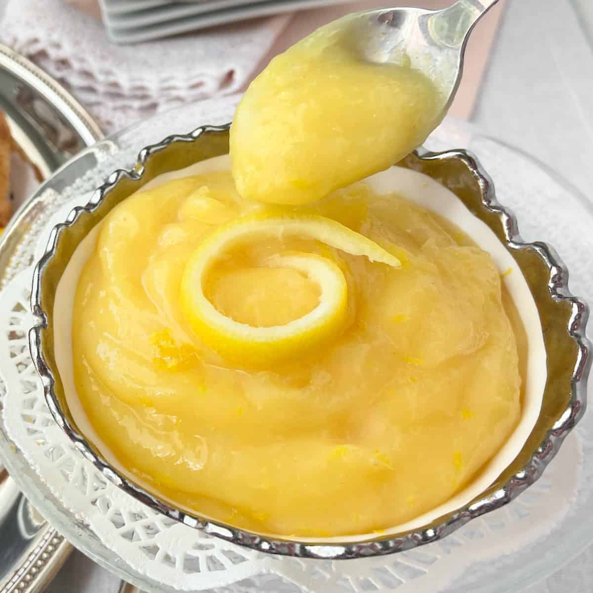 Lemon curd on a spoon in an antique silver lined serving bowl.